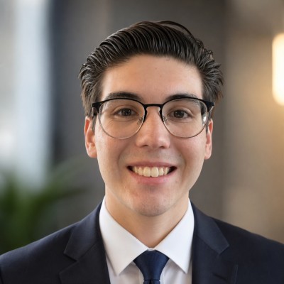 Tanner Rivera smiling, wearing glasses and a suit
